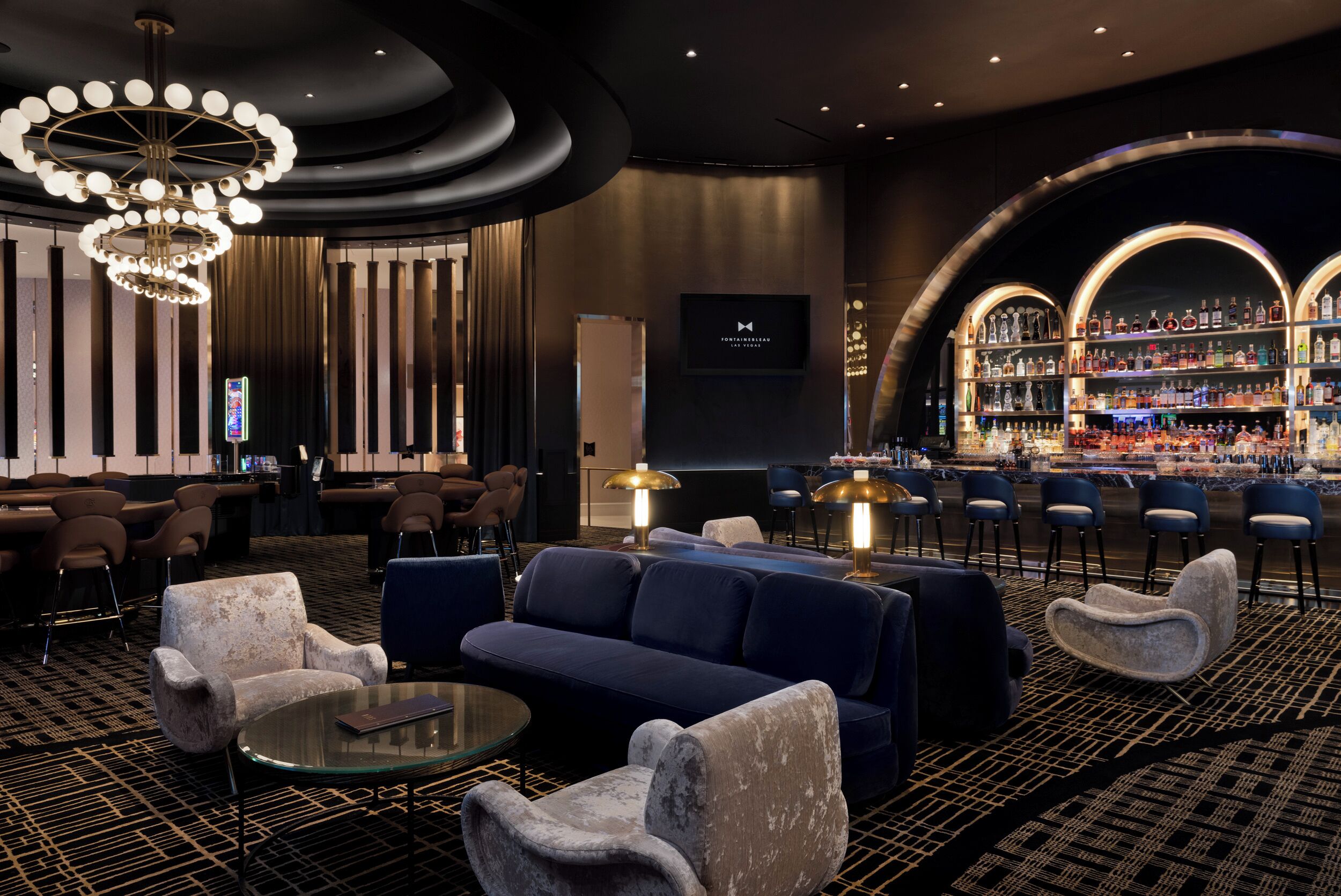A modern lounge area with sofas, armchairs, and a bar with shelves of bottles.