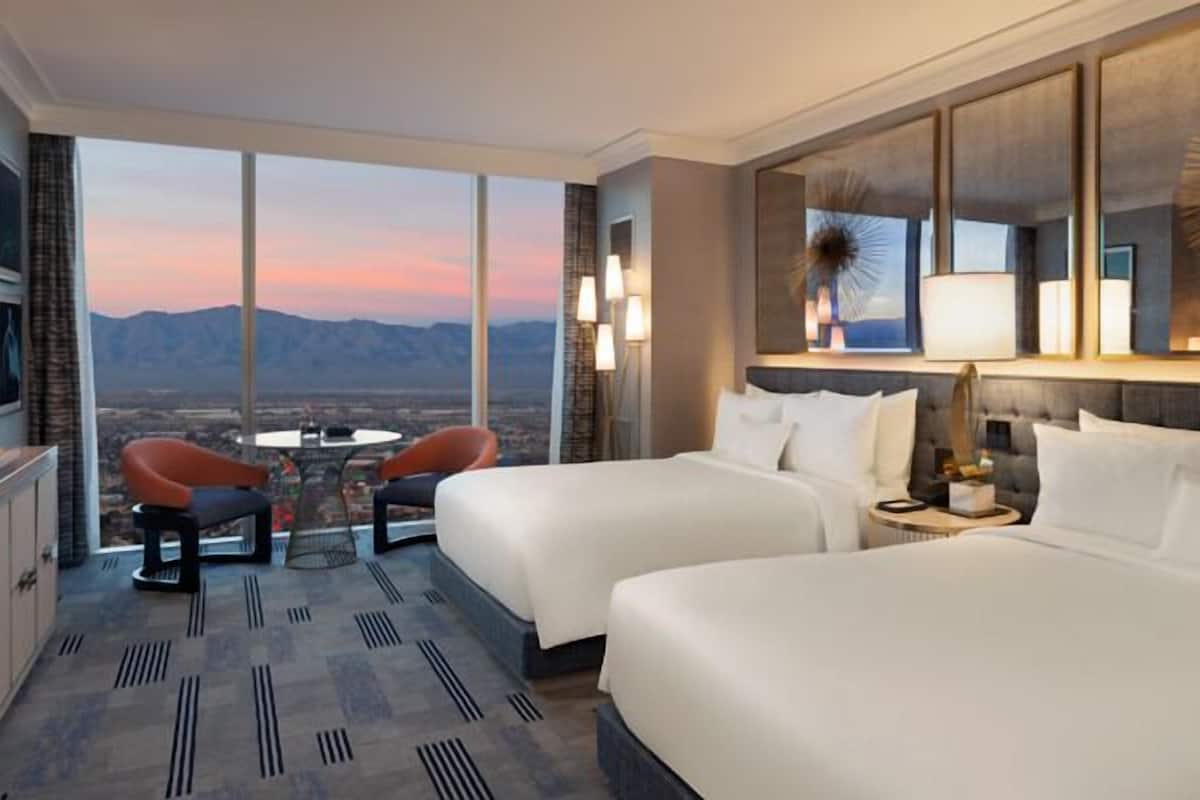 Une chambre d’hôtel avec deux lits, une table à manger avec des chaises et une vue sur les montagnes.