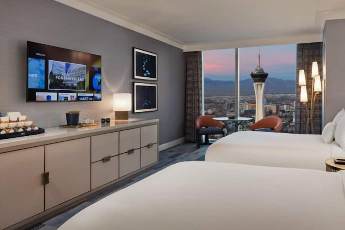 Une chambre d’hôtel avec deux lits, une télévision, un bureau équipé et une vue sur la ville, avec une tour en particulier.