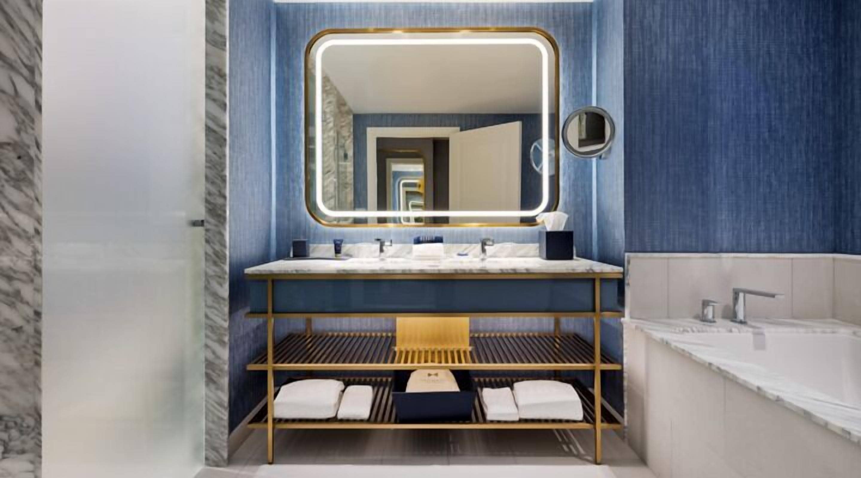 Un baño moderno con pared de mármol, tocador con espejo, bañera y estante con toallas.