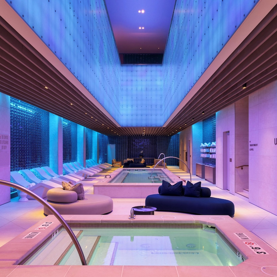 A modern spa area with a large hot tub, seating, and a ceiling with a unique light pattern.