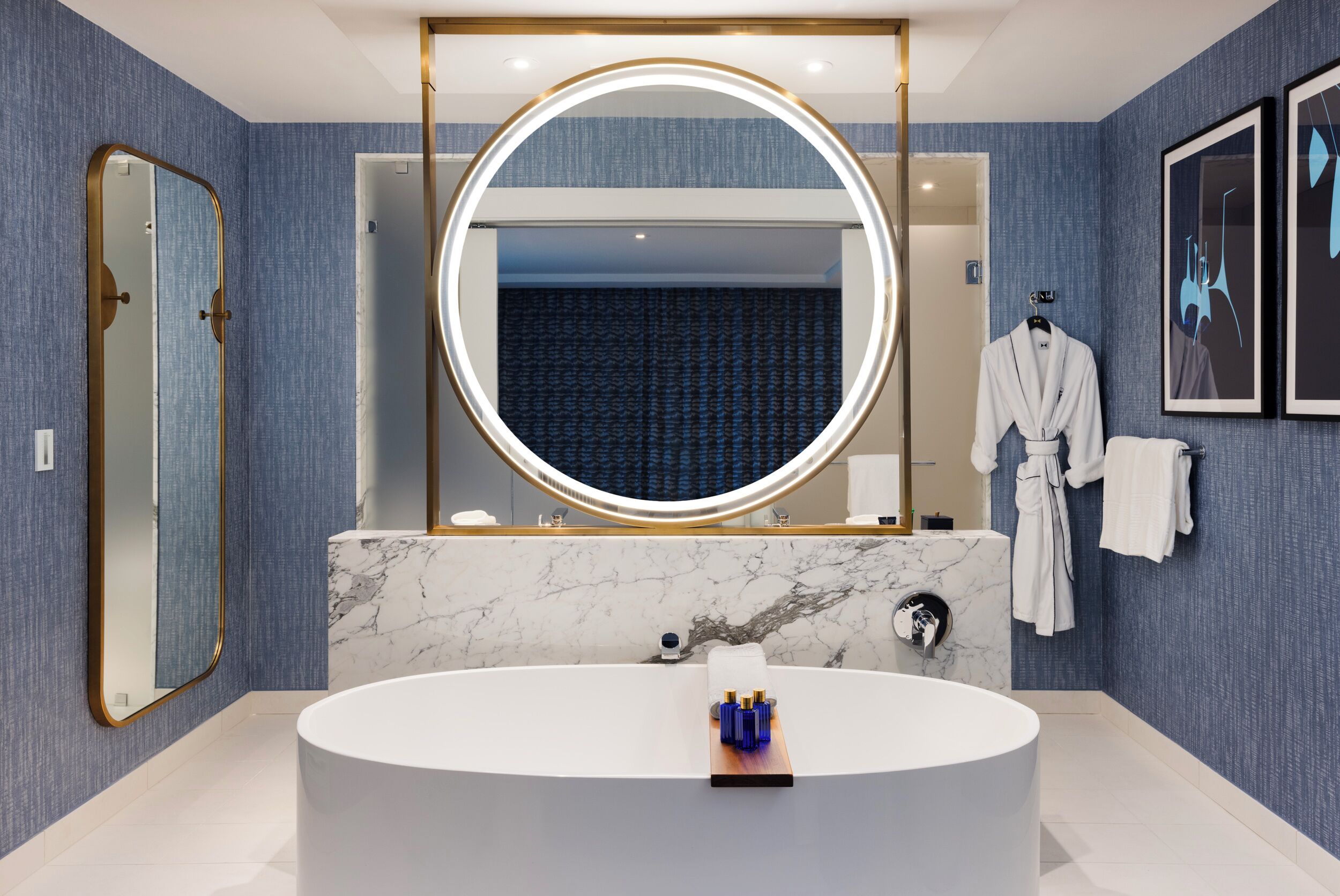 A modern bathroom with a large oval sink, a round mirror with a light, and a robe hanging on a rack.