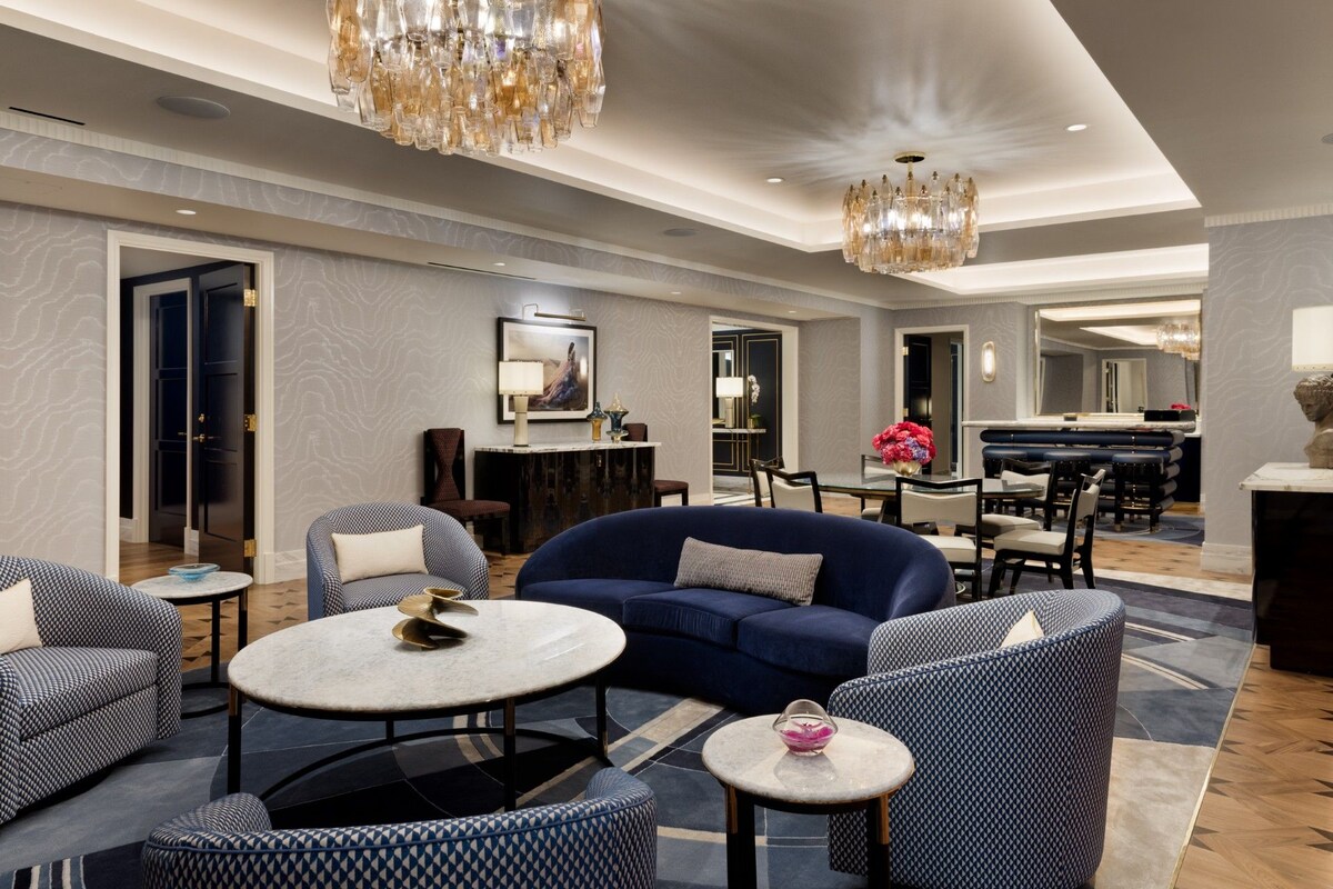 Een moderne hotellobby met een blauwe bank, gestreepe fauteuils, een ronde tafel en een kroonluchter.