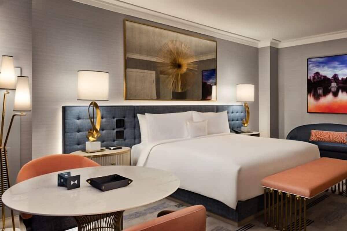 Une chambre d’hôtel moderne avec un grand lit, une table de salle à manger ronde, un canapé et un banc.