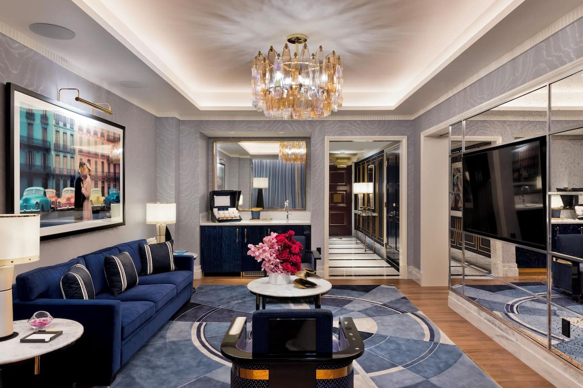 Un hall d’hôtel moderne avec un canapé bleu, une table basse ronde, un lustre et un grand miroir.