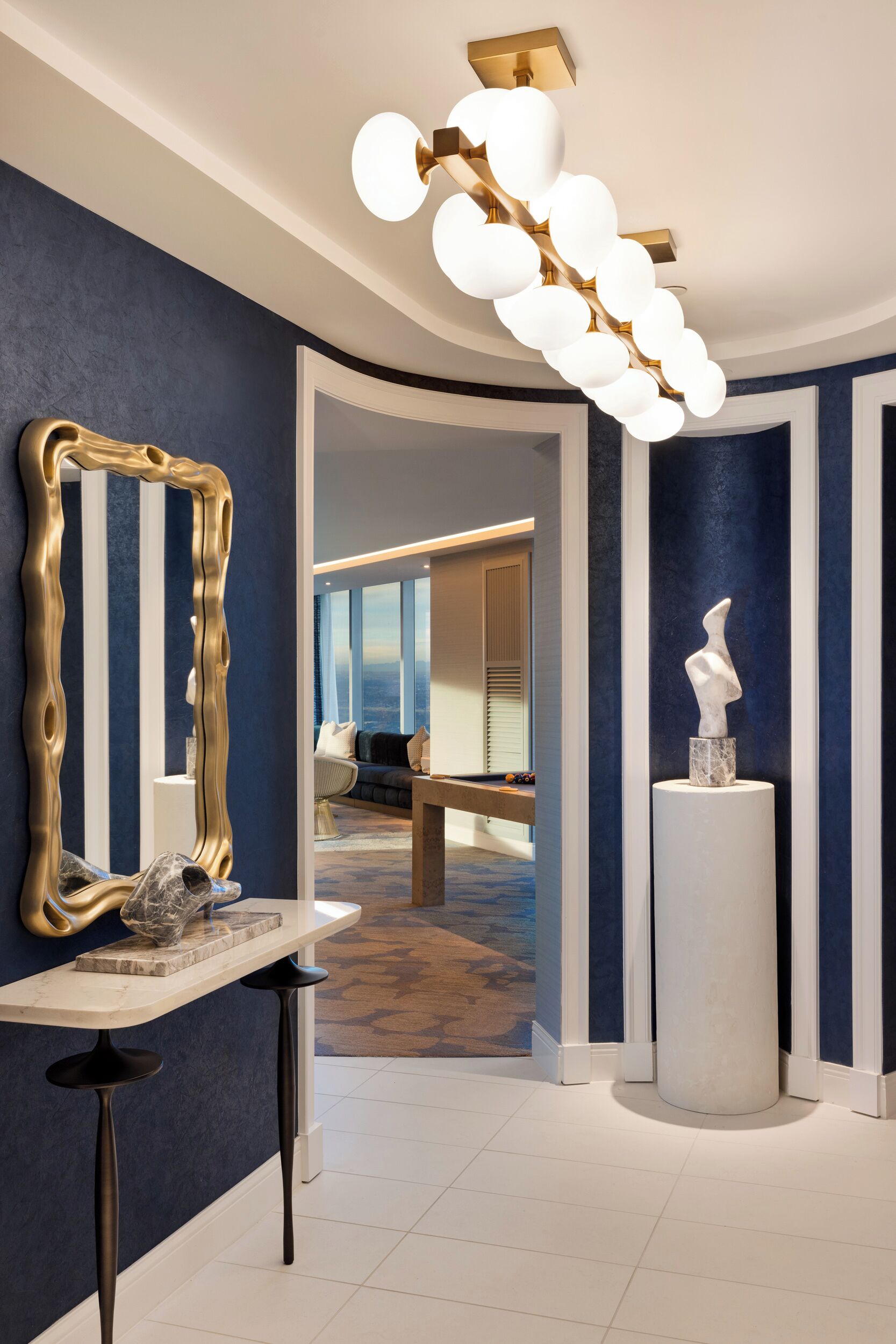 Een modern interieur met een marmeren console tafel, een grote spiegel met gouden lijst en een bijzondere plafondlamp.
