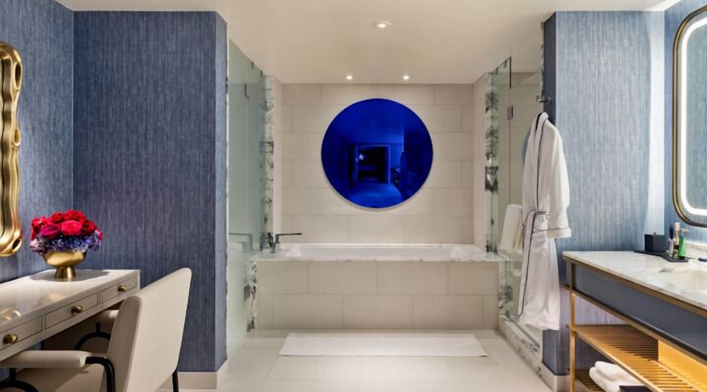 Un baño moderno con una bañera grande, un tocador con un jarrón dorado y un espejo redondo en la pared.