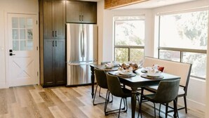 Une cuisine moderne avec des meubles de couleur sombre, des appareils en acier inoxydable et une table à manger pour quatre personnes.