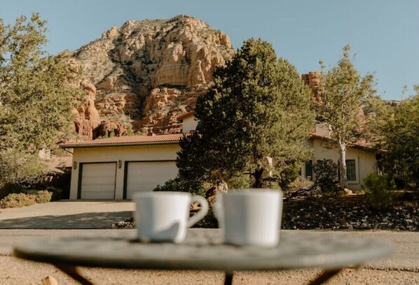 Una casa con garaje, una montaña al fondo y dos tazas blancas sobre una mesa.