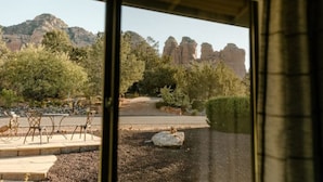 On voit une zone dallée avec quelques chaises et une table, un rocher et un sentier menant à un paysage naturel parsemé de formations rocheuses.