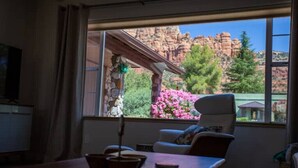 Quarto com uma grande janela com vista para uma paisagem montanhosa, uma mesa de madeira com uma tigela e uma cadeira.