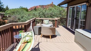 Um deck de madeira com móveis de exterior, incluindo uma rede, uma cadeira de vime e uma mesa pequena.