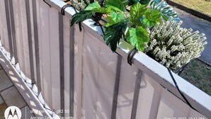 Un balcon orné de plantes en pot, une poubelle bleue et une poubelle jaune.