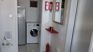 Une cuisine de taille réduite équipée d’un lave-linge, d’un extincteur rouge et d’une cuisinière.