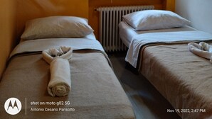 Une chambre d’hôtel avec deux lits, une fenêtre avec des stores et deux tableaux colorés accrochés au mur.