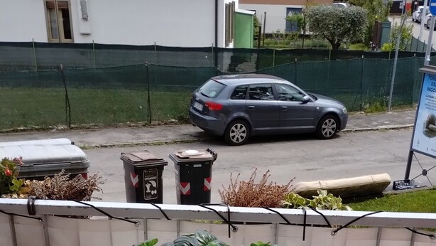Un balcon avec une table blanche et deux chaises rouges, un pot de fleurs et une vue sur la rue.