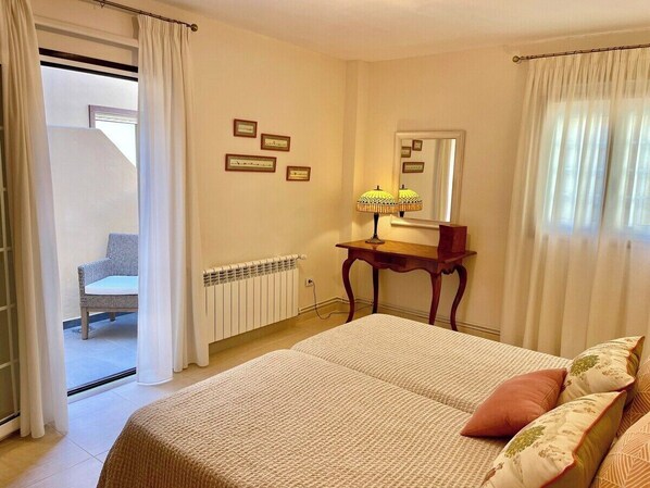 A bedroom with a bed, a bedside table with a lamp, a chair, and a view of a balcony.