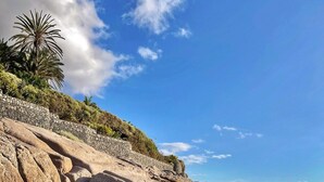 Ein Strand mit großen Felsen, blauem Himmel und ruhiger See.