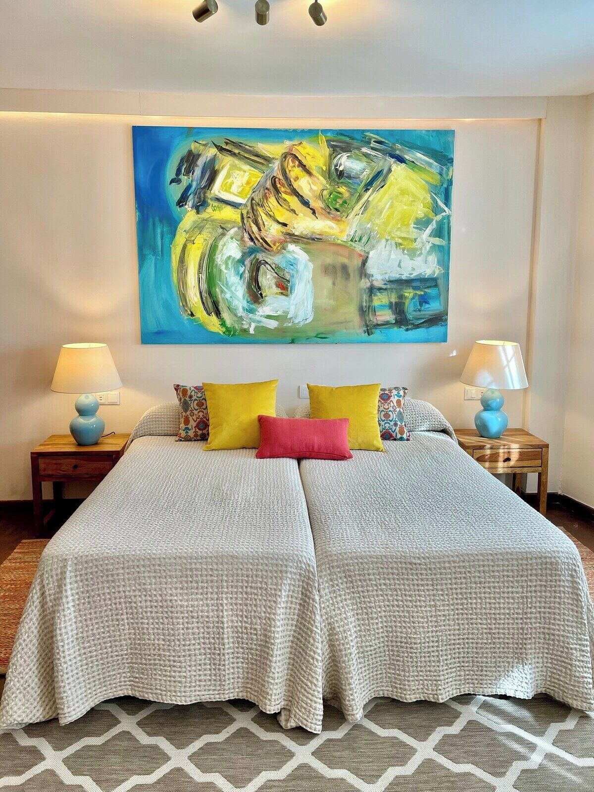 A double bed with two pillows, a large abstract painting above, and two bedside lamps on wooden nightstands.