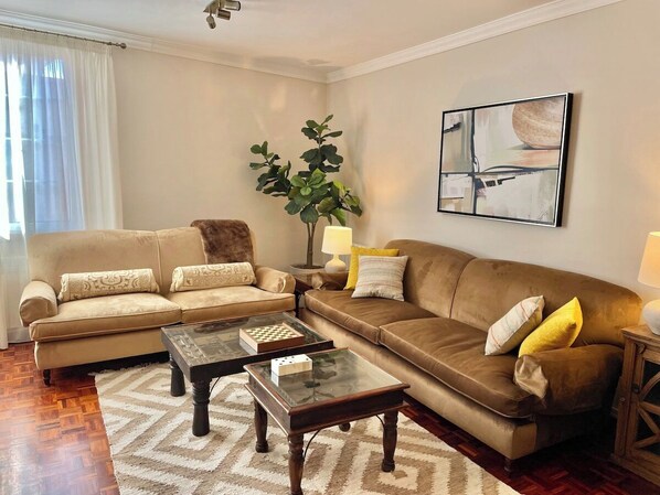 A living room with a beige sofa, a brown sofa, a glass coffee table, and a lamp.