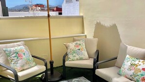 Eine Dachterrasse mit zwei weißen Sofas, einem Tisch mit Gläsern und einem Strohdachschirm.
