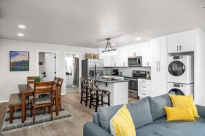 Una cocina moderna con armarios blancos, una isla central y un comedor con mesa y sillas.