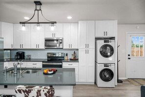 Una cocina moderna con armarios blancos, un lavamanos de acero inoxidable, un microondas y lavadora y secadora integradas.