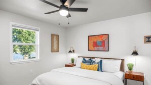 Een slaapkamer met een bed, een plafondventilator, een raam en kunstwerken aan de muren.