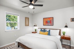 A bedroom with a bed, a ceiling fan, a window, and artwork on the walls.