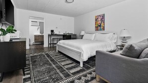 A modern hotel room with a bed, a desk, a chair, a TV, and a painting on the wall.