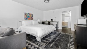 A modern hotel room with a bed, a desk, a chair, a TV, and a painting on the wall. - Apartment close to downtown, beaches, and wineries (Traverse City)