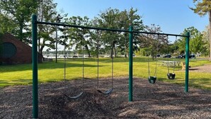 A playground with swings and a brick building in the background. - Close to Beaches and Downtown (Traverse City)