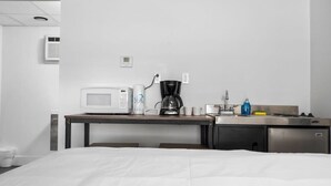 A hotel room with a bed, a small kitchenette with a microwave, coffee maker, and sink. - Peninsula One Apartments Unit 4 (Traverse City)