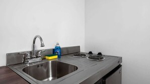 Una cocina con un lavamanos de acero inoxidable, un grifo, una estufa y una botella de detergente para lavar platos.