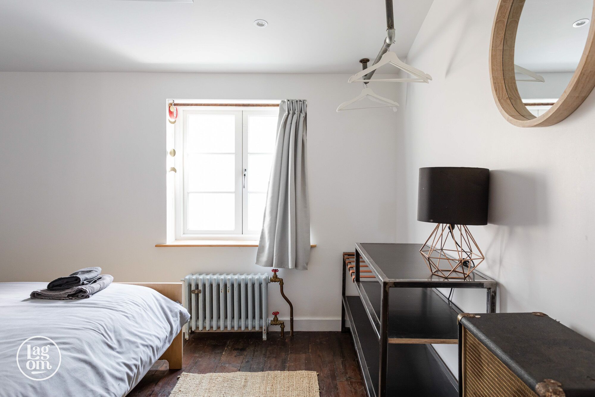 A bedroom with a bed, radiator, desk, lamp, and a mirror on the wall.