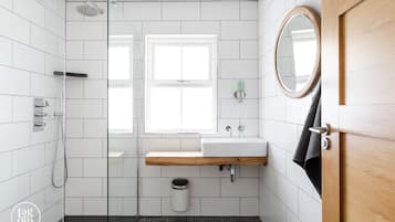 Un baño moderno con azulejos blancos, cabina de ducha de cristal, tocador de madera y un ventanal.