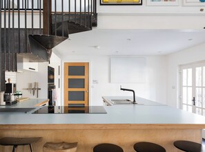 Une cuisine moderne dotée d’un îlot central, d’un four encastré et d’une porte en bois.