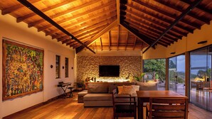 A spacious living area with a stone wall, wooden ceiling, and a large TV. - Casa Mirador Boutique Hotel (Búzios)