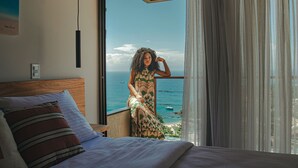 A bedroom with a large bed, a view of the sea, and a balcony with a person. - Casa Mirador Boutique Hotel (Búzios)