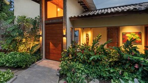 A modern house with a wooden front door, a tiled roof, and a well-maintained garden with various plants and a pathway leading to the entrance. - Casa Mirador Boutique Hotel (Búzios)