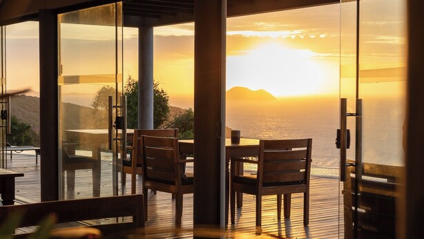 A dining area with a view of the sunset over the ocean, featuring a wooden table and chairs. - Casa Mirador Boutique Hotel (Búzios)
