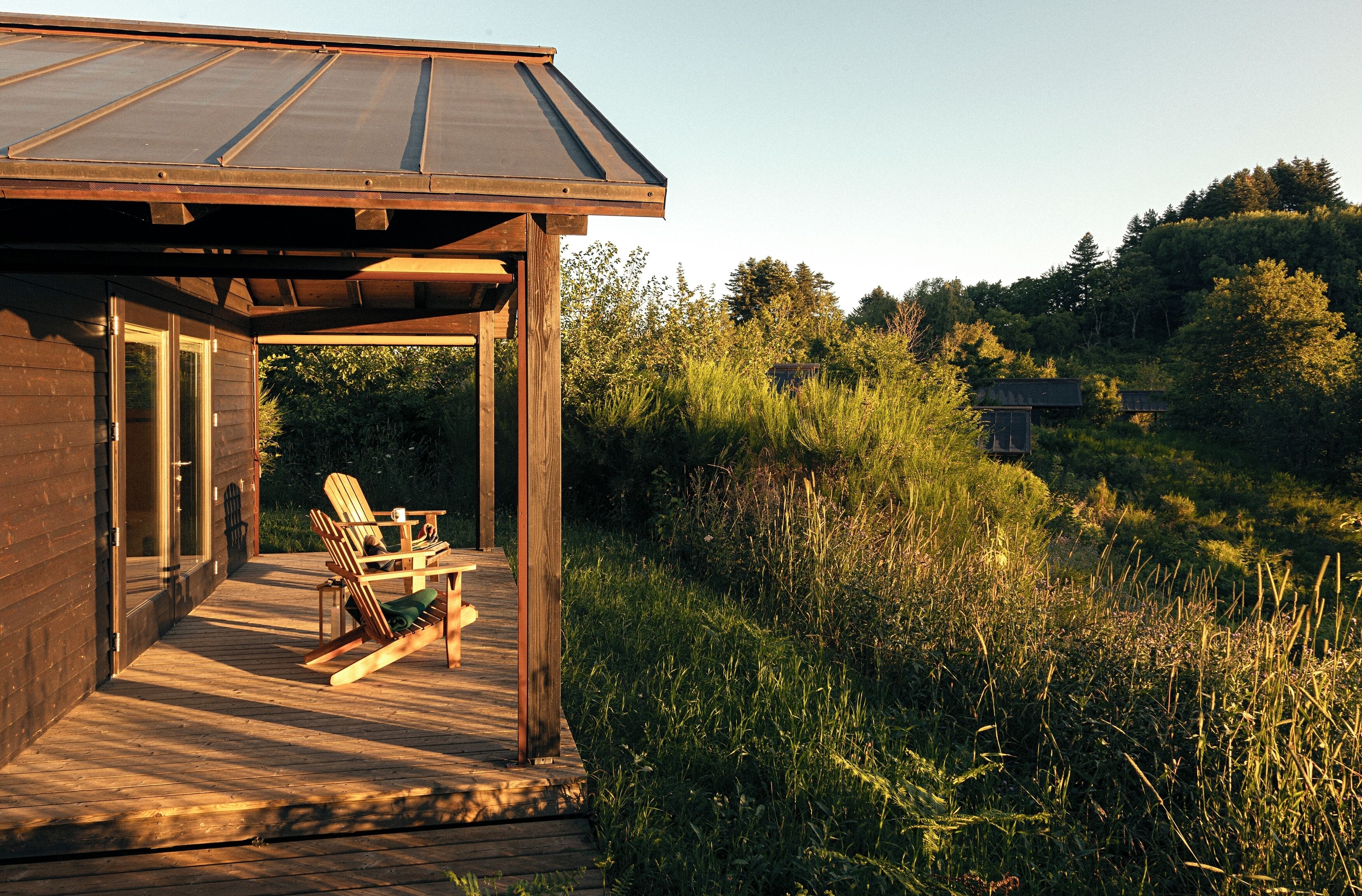 A wooden cabin with a deck, outdoor seating, and a view of the surrounding forest.