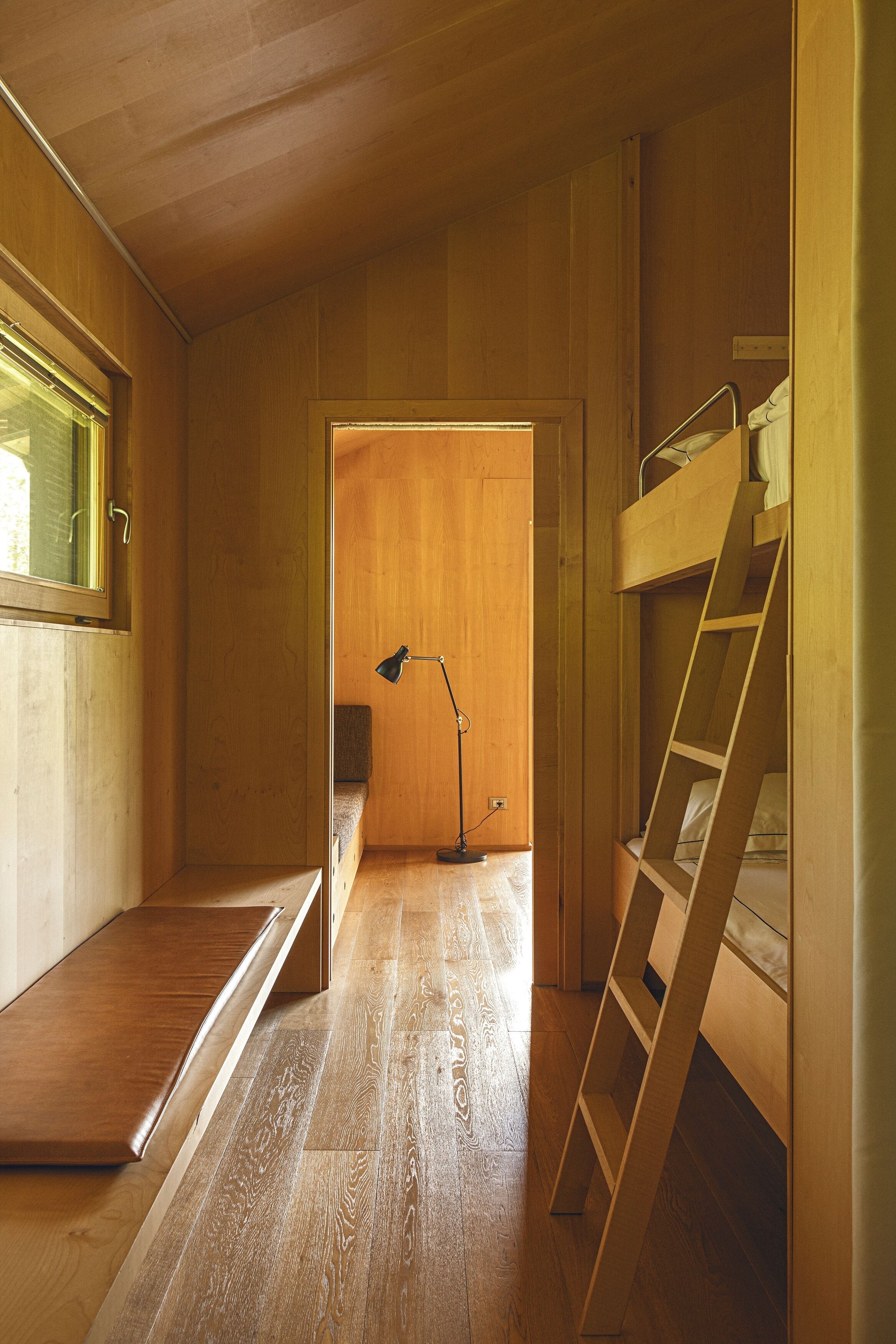 Quarto pequeno com beliche, escada, escrivaninha e janela.