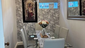 Un espace repas avec une table en verre, des chaises blanches, un lustre et des murs à motifs de marbre.