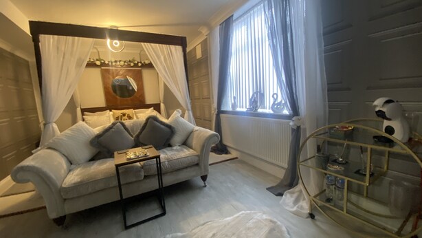 Une chambre moderne avec un canapé blanc, une table basse en verre, un tapis en fourrure, une table de chevet, un miroir et une fenêtre avec des rideaux.