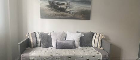 Un dormitorio con un sofá cama gris, una pared blanca y un cuadro de un barco en la pared.