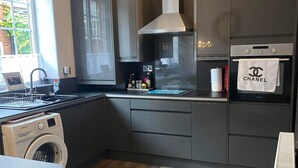 Une cuisine moderne avec des meubles gris, un four encastré, un lave-linge et une fenêtre qui laisse entrer la lumière naturelle.