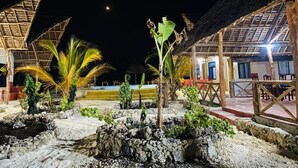 A nighttime view of a resort with thatched-roof structures, palm trees, and a pool area. - MKEKA SPICE LODGE (Jambiani)