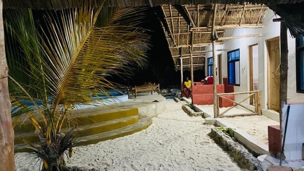 A sandy pathway leading to a building with a thatched roof, a palm tree, and a small pool. - MKEKA SPICE LODGE (Jambiani)
