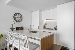 Une cuisine moderne avec des meubles blancs, un îlot central doté de sièges, une horloge murale et une petite orchidée en pot.